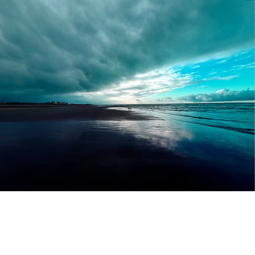 Strand met de zee aan de rechterkant. De lucht is dramatisch met donkere wolken aan de linkerkant en lichtere, helderblauwe lucht aan de rechterkant.