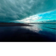 Strand met de zee aan de rechterkant. De lucht is dramatisch met donkere wolken aan de linkerkant en lichtere, helderblauwe lucht aan de rechterkant.