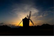 Silhouet van een houten windmolen tekent zich af tegen een kleurverloop van diepblauw naar oranje aan de horizon.