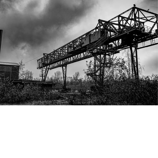 Zwart-witfoto van een grote metalen kraanconstructie op een verlaten terrein.