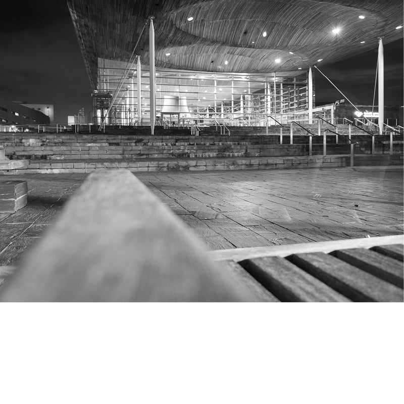 Zwart-witfoto van een modern gebouw met glazen gevel en trappen, ’s nachts verlicht.