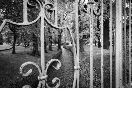 Zwart-witfoto van een sierlijk ijzeren hek met zicht op een park en kronkelende beek.