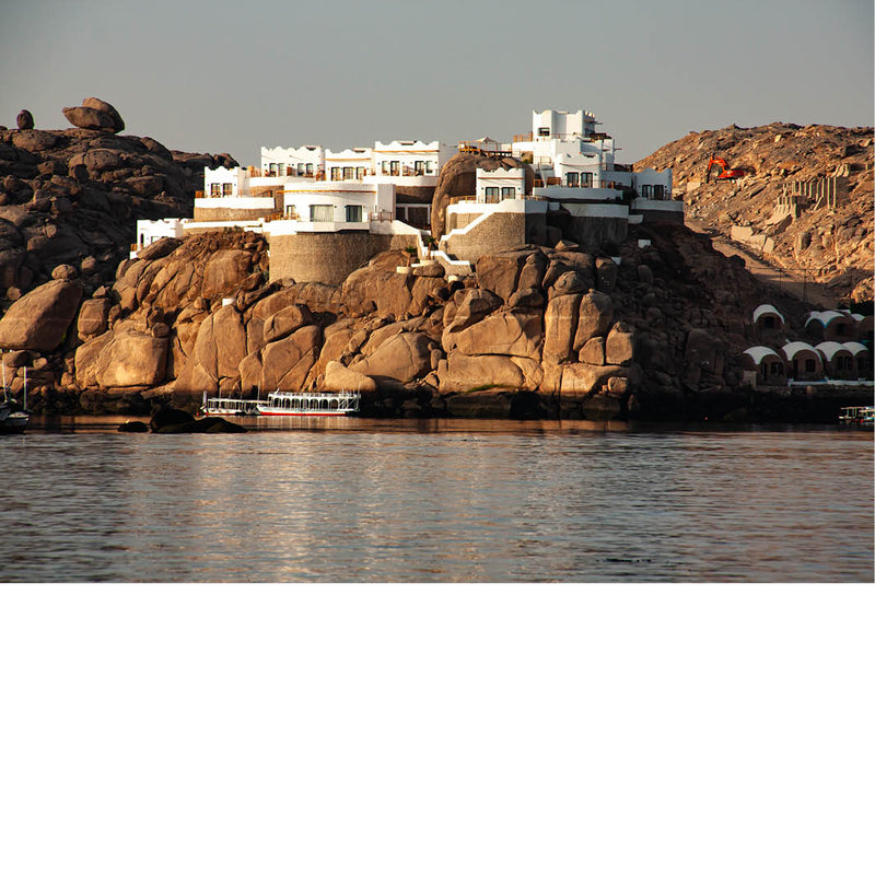 Foto van witte gebouwen op een rotsachtige kustlijn, met kalm water op de voorgrond.