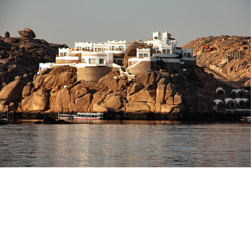 Foto van witte gebouwen op een rotsachtige kustlijn, met kalm water op de voorgrond.