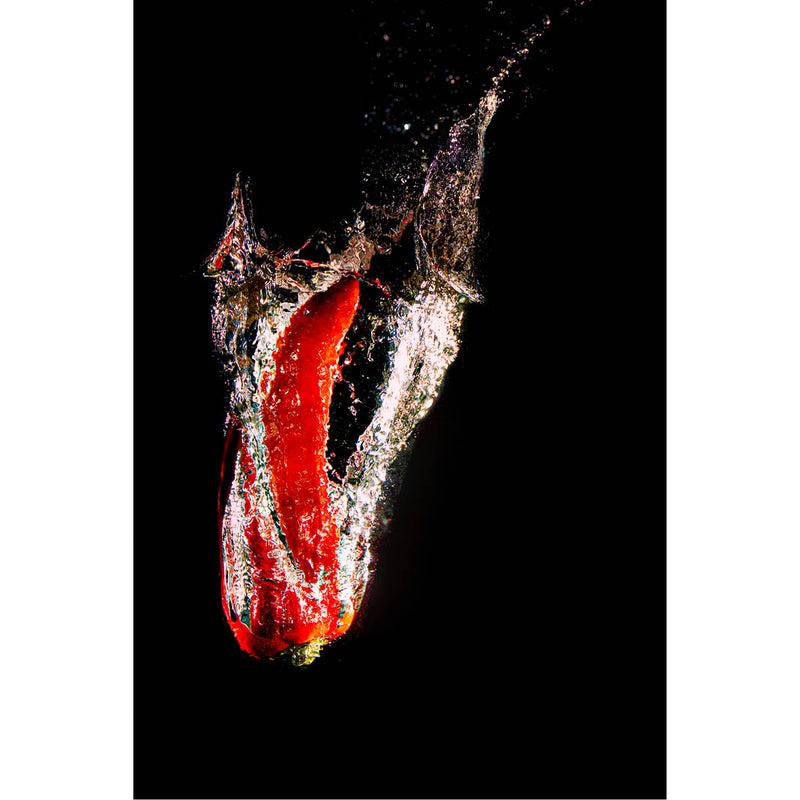 Close-up van een rode paprika die in water valt, met dynamische spetters tegen zwarte achtergrond.