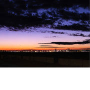 Foto van een kleurrijke avondlucht met paarse en oranje tinten boven een haven met verlichte kranen.