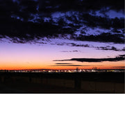 Foto van een kleurrijke avondlucht met paarse en oranje tinten boven een haven met verlichte kranen.