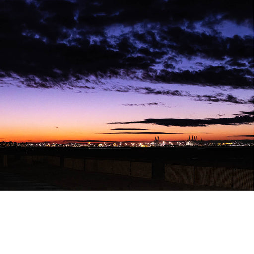 Foto van een kleurrijke avondlucht met paarse en oranje tinten boven een haven met verlichte kranen.