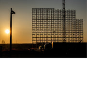 Foto van een metalen constructie in silhouet tegen een warme zonsopgang, met zon laag aan de horizon.