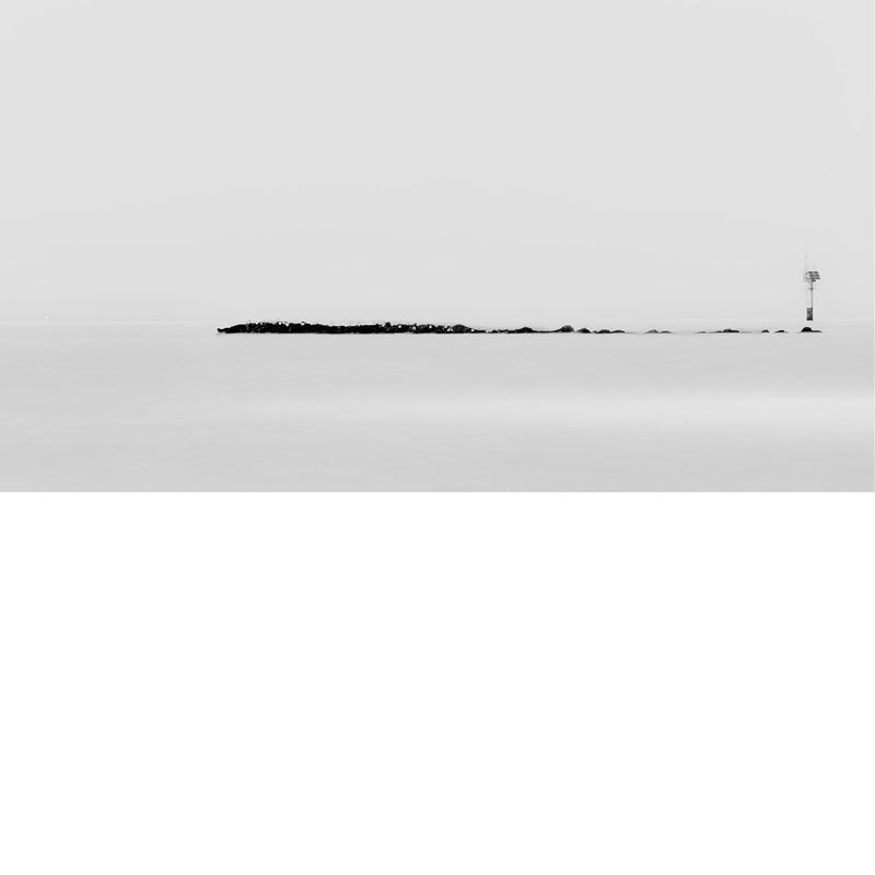 Artistieke zwart-witfoto van een kustlijn met een lange golfbreker en een navigatiepaal, vastgelegd in minimalistische stijl.