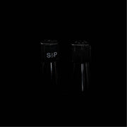 Een minimalistische low-key opname van twee slanke peper- en zoutvaatjes die subtiel uit de diepe zwarte achtergrond tevoorschijn komen. 