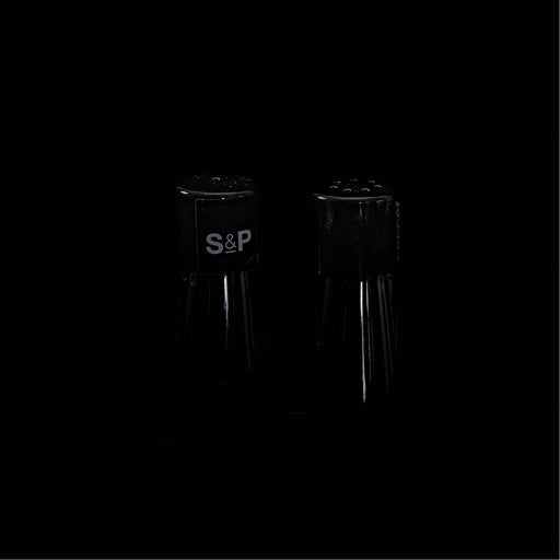 Een minimalistische low-key opname van twee slanke peper- en zoutvaatjes die subtiel uit de diepe zwarte achtergrond tevoorschijn komen. 