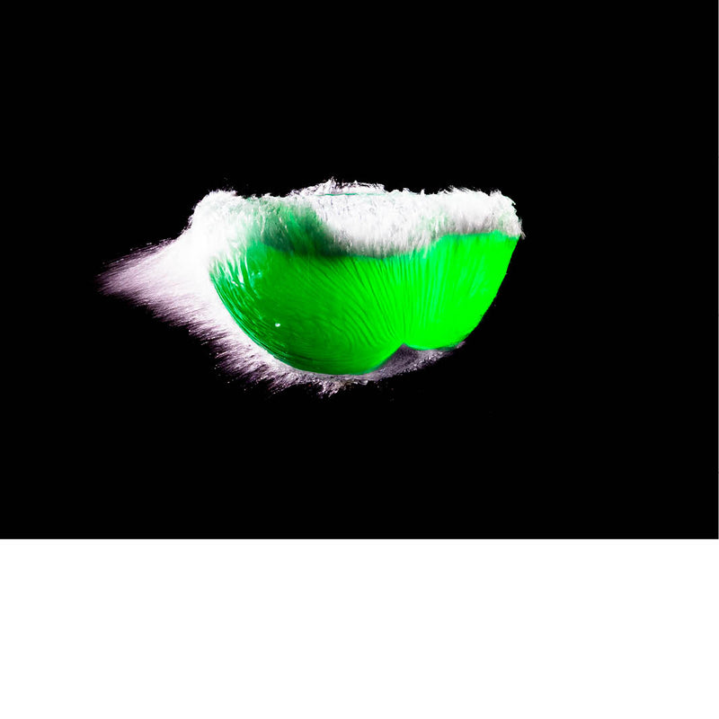 Een felgroene ballon spat open in een fractie van een seconde, vastgelegd op het exacte moment waarop oppervlaktespanning en explosieve beweging elkaar kruisen. 