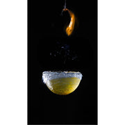 Een felgele watermassa blijft nog heel even in vorm hangen terwijl de ballon eromheen in een fractie van een seconde uit elkaar spat. De bovenste fragmenten van het ballonrubber bewegen als een lichtgevende sliert omhoog, terwijl het water onderaan een gladde, bijna glasachtige halve bol vormt. 