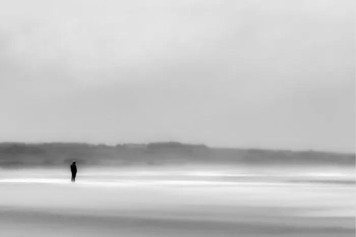 Kleine silhouet van een wandelaar op het wijde, nevelige strand van Wissant, waar zand, zee en lucht in zachte grijstinten in elkaar overlopen.
