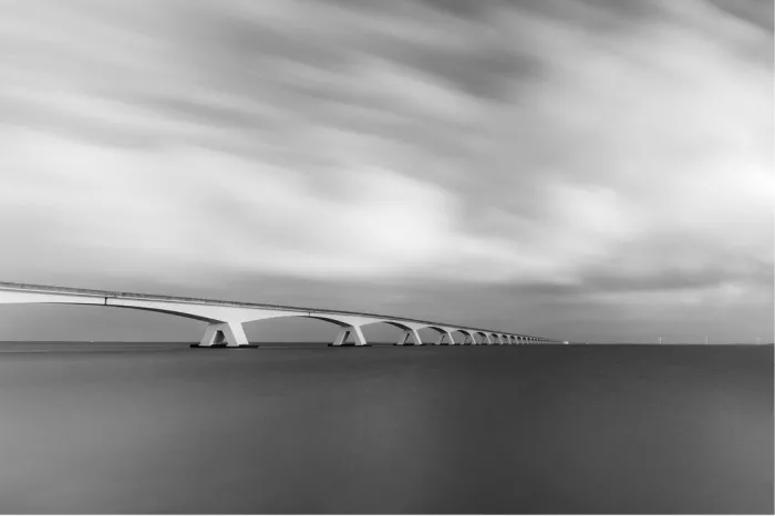 Zeelandbrug met een lange rij bogen die naar de horizon loopt boven glad water, onder gestreepte wolken