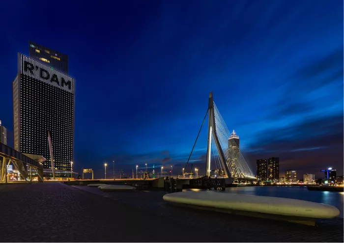 Erasmusbrug en verlichte toren met het opschrift R'DAM onder een diepblauwe avondlucht met gestreepte wolken