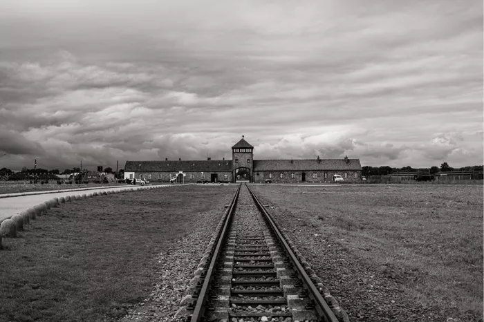 Spoorlijn die recht naar het poortgebouw van Auschwitz-Birkenau loopt, onder een grijze wolkenlucht