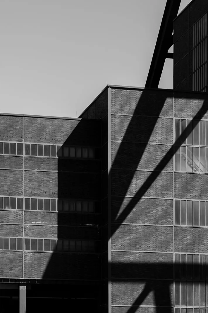 Bakstenen industriële gevel met rijen vensters, doorsneden door de diagonale schaduw van een stalen constructie