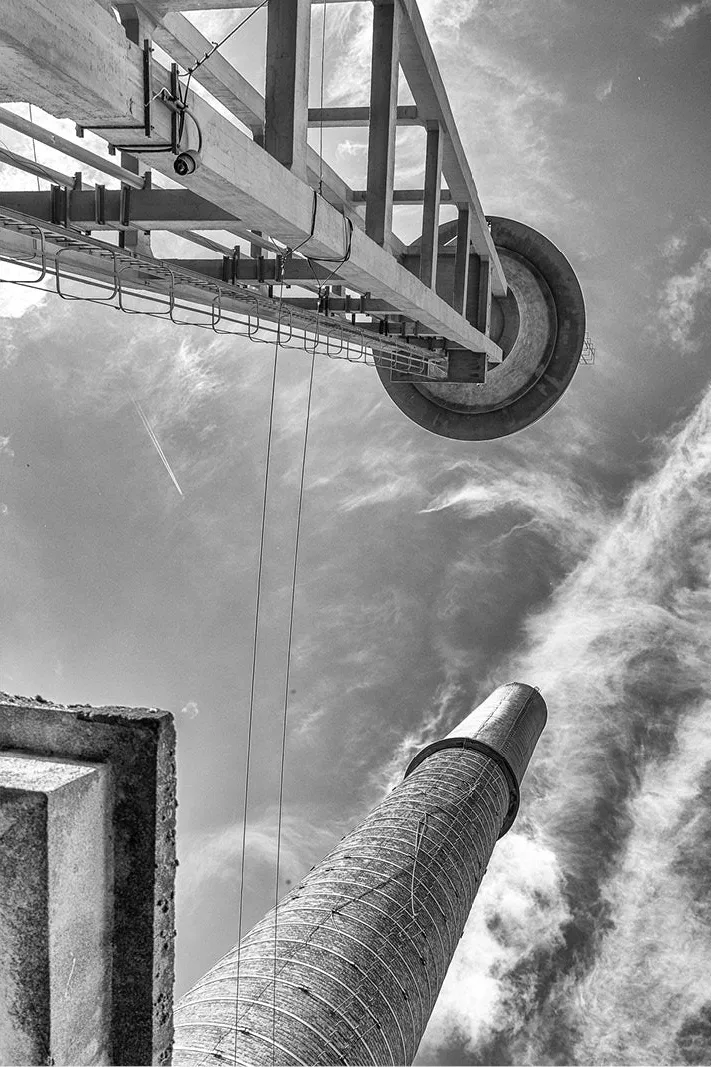 Stalen brugconstructie en hoge bakstenen schoorsteen schuin van onderen gezien tegen sluierwolken