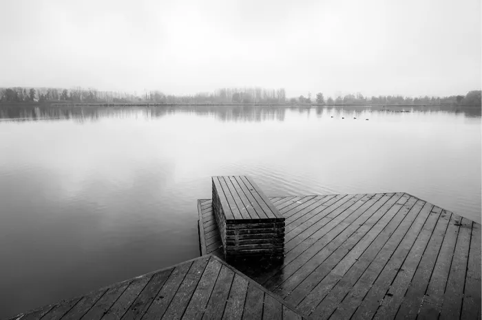Houten vlonder met rustbank aan een kalm meer, met een rij bomen aan de overkant