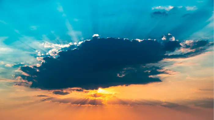 Donkere wolk voor de zon met zonnestralen in een blauwe en oranje lucht