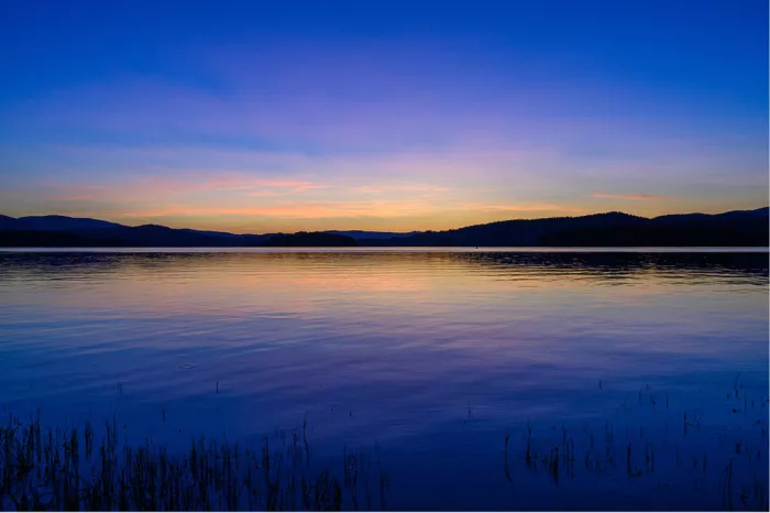 Meer in het blauwe uur met een oranje streep zonsondergang boven donkere heuvels