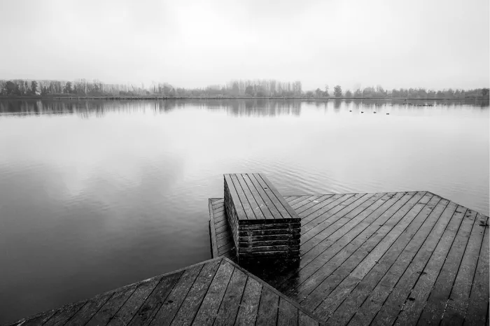Houten steiger met zitbank aan een mistig meer in zwart-wit