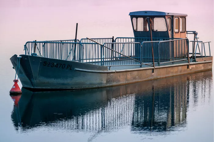 Verweerde boot met stalen reling en cabine, gespiegeld in roze getint water