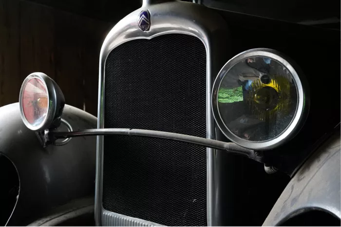 Radiatorrooster en twee koplampen van een Citroën oldtimer, links roze, rechts geel en groen, tegen een donkere achtergrond.