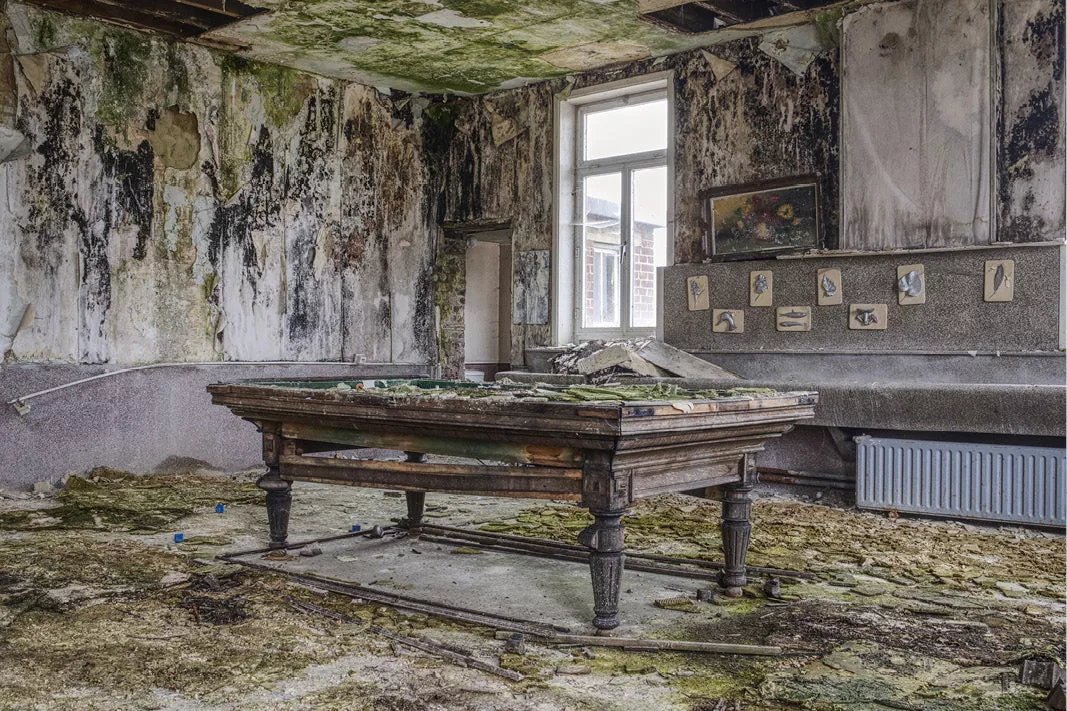 Oude biljarttafel in een vervallen kamer met schimmel en mos op de muren, een raam en een radiator op de achtergrond