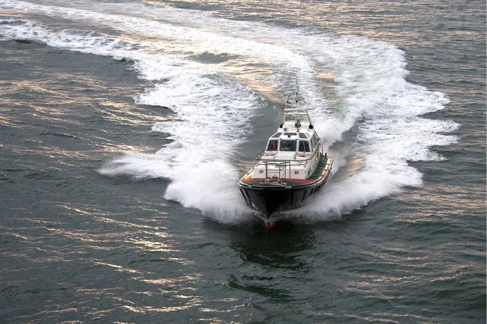 Loodsboot vaart met hoge snelheid op de kijker af, met een witte boeggolf en een kielzog in een bocht