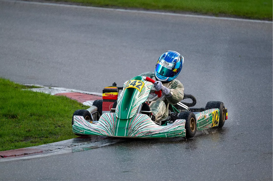 Kartracer met blauwe helm in een groene kart met nummer 242 neemt een bocht op een natte baan