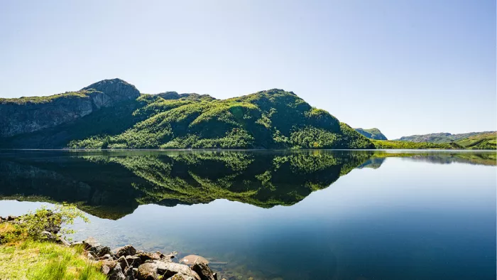 Groene bergrug spiegelt in een glad meer met rotsblokken aan de oever