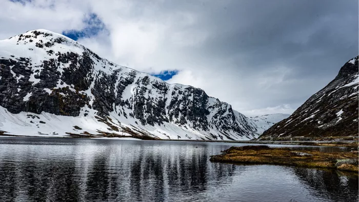 Besneeuwde bergwand spiegelt in een stil meer onder een wolkenlucht