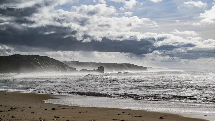 Strand met ruwe golven en donkere kliffen onder zware wolken in grijstinten