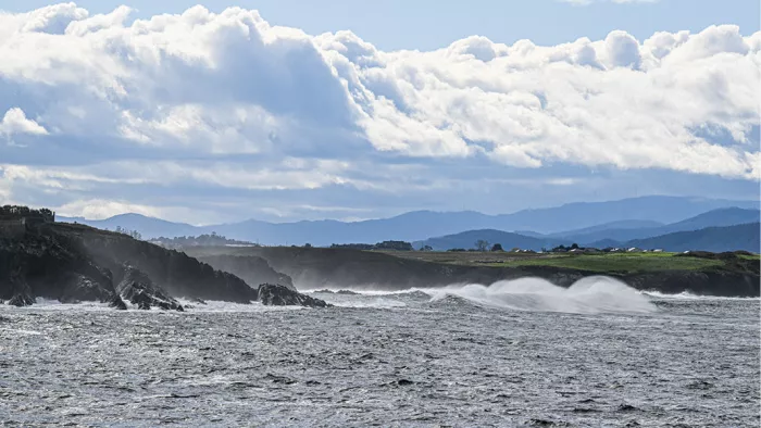 Woelige zee met golven die door de wind wegwaaien voor een rotskust met bergen