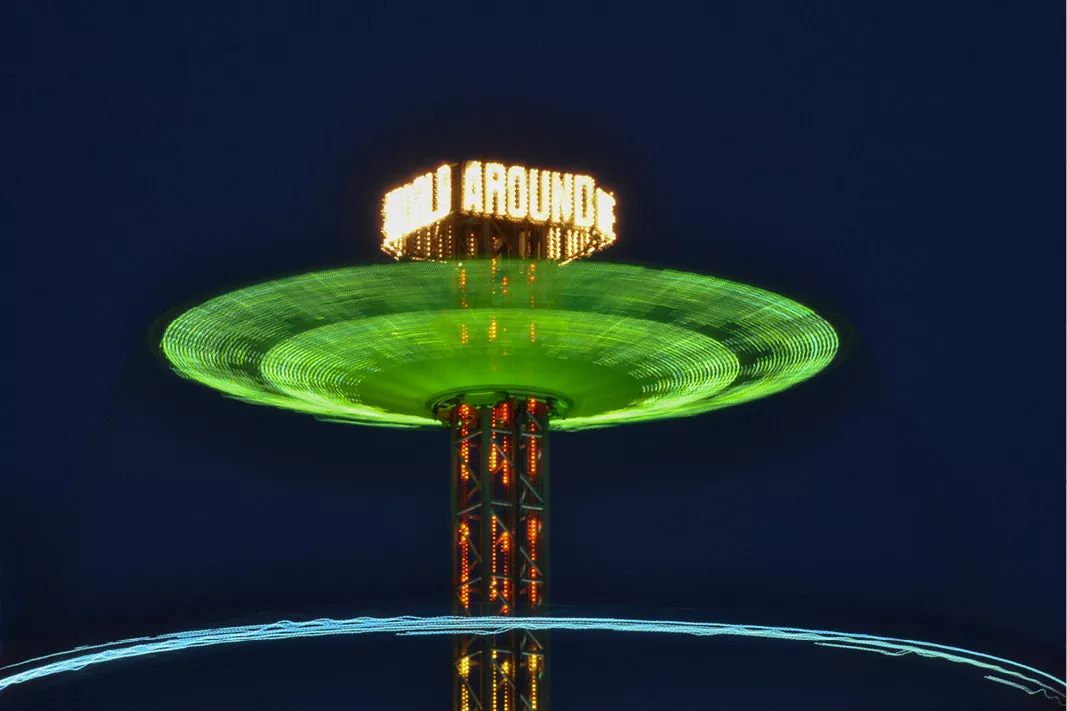 Draaiende kermisattractie vormt een groene lichtschijf rond een verlichte toren