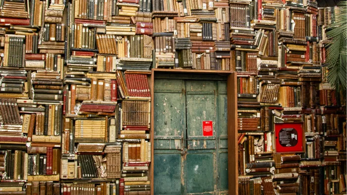 Muur van opgestapelde oude boeken rond een verweerde groenblauwe deur