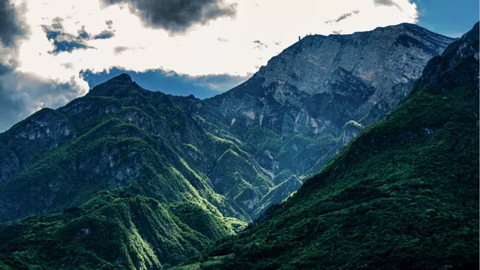 Beboste berghellingen en een grijze bergtop onder donkere wolken