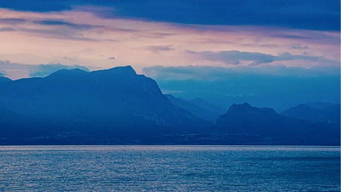 Blauwe bergsilhouetten boven een meer met een roze gekleurde lucht