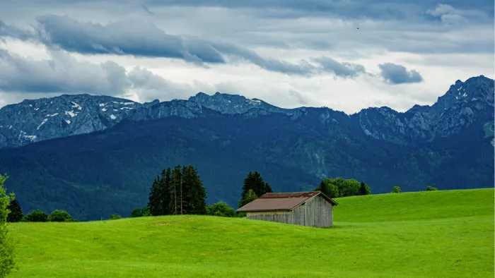 Houten stal op een groene weide voor beboste bergen onder wolken