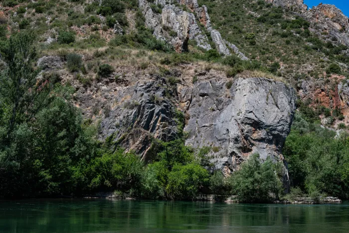 Grijze rotsen en groene struiken aan de oever van een kalme rivier