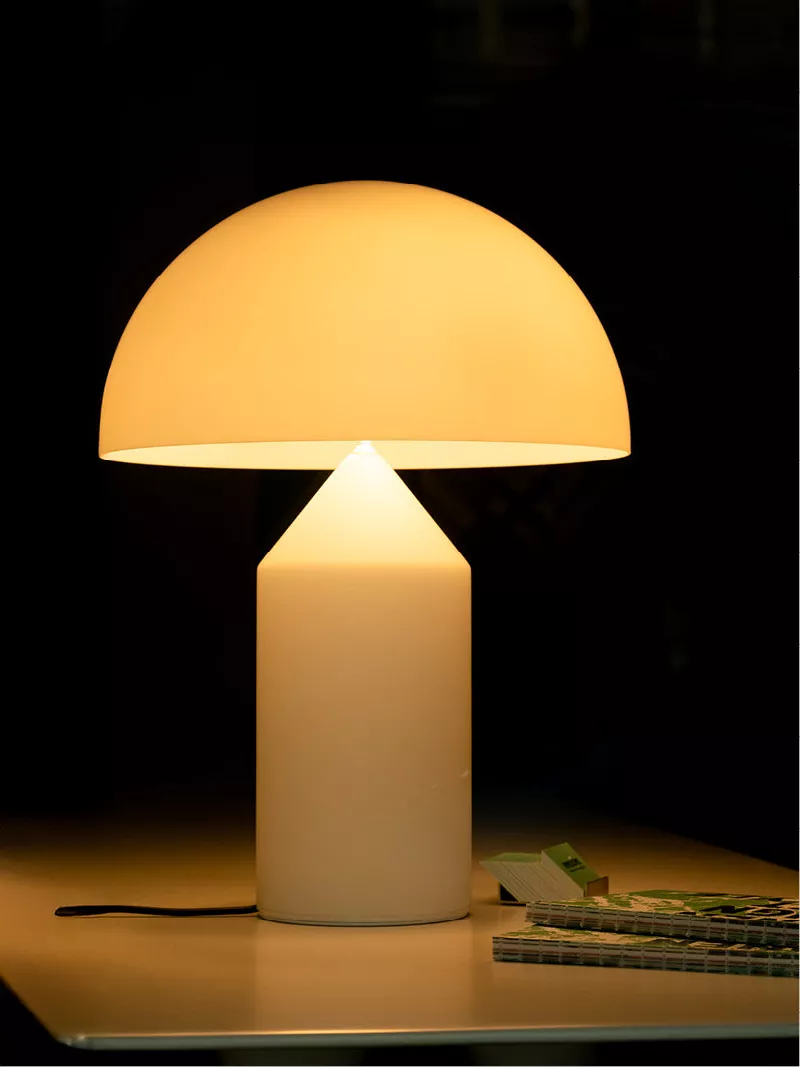 Paddenstoelvormige tafellamp met warm licht in een donker interieur, met een boekje op tafel