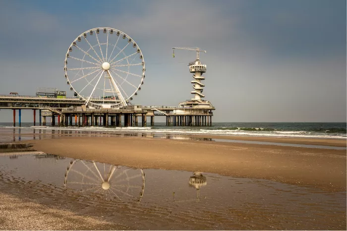 Pier met reuzenrad en uitkijktoren weerspiegelt in een plas op het natte strand