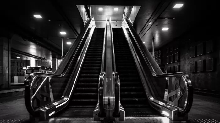 Twee lege roltrappen in een donker station, met glanzende leuningen en vierkante lichtpunten in het plafond.
