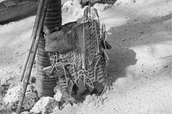 Gevlochten visfuik met touwtjes tegen een paal op zand, met bamboestokken ernaast