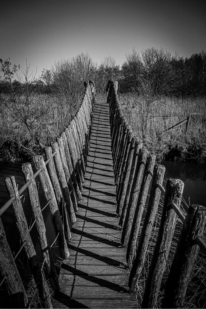 Een houten hangbrug over de rivier de Dommel in het Belgische natuurpark Hageven in Pelt. De zon zorgde voor een mooi schaduwspel op het hout, dat bovendien een fraai reliëf heeft.