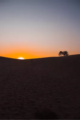 De zon verdwijnt achter een zandduin, de foto