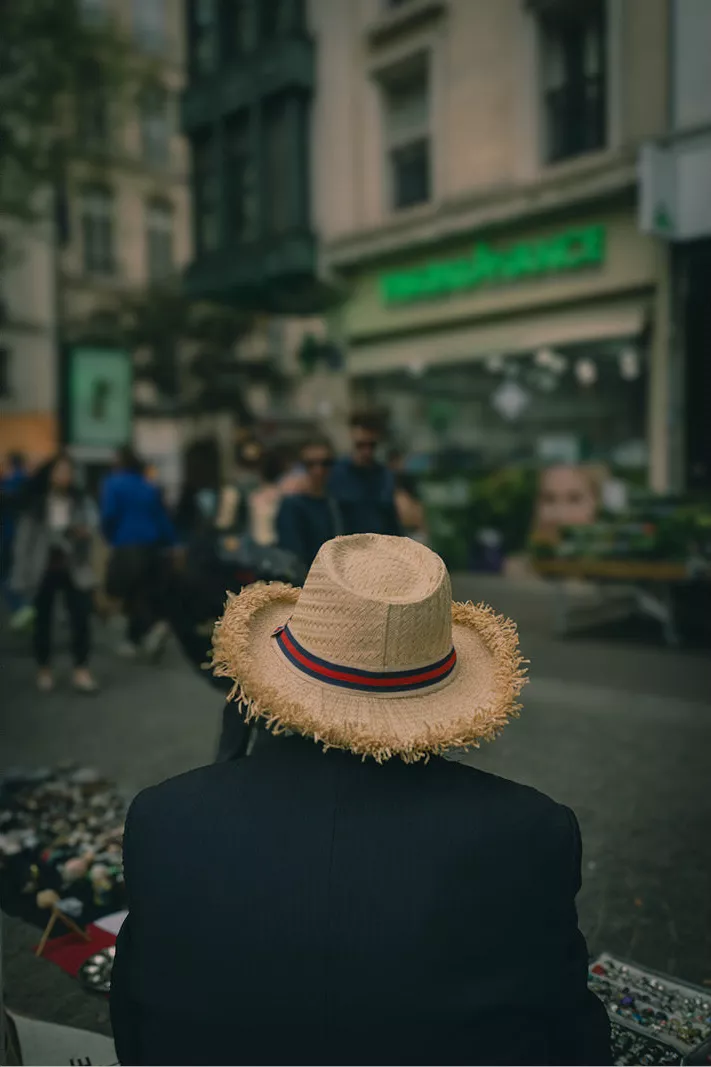 Een oude straatverkoper langs een straat in het drukke Parijs. Van onder zijn strohoed lacht hij de voorbijgangers minzaam toe. Ze vormen mee het decor, hij is de enige vaste waarde in dit beeld. Deze foto nam ik in de levendige wijk 'Le Marais'.